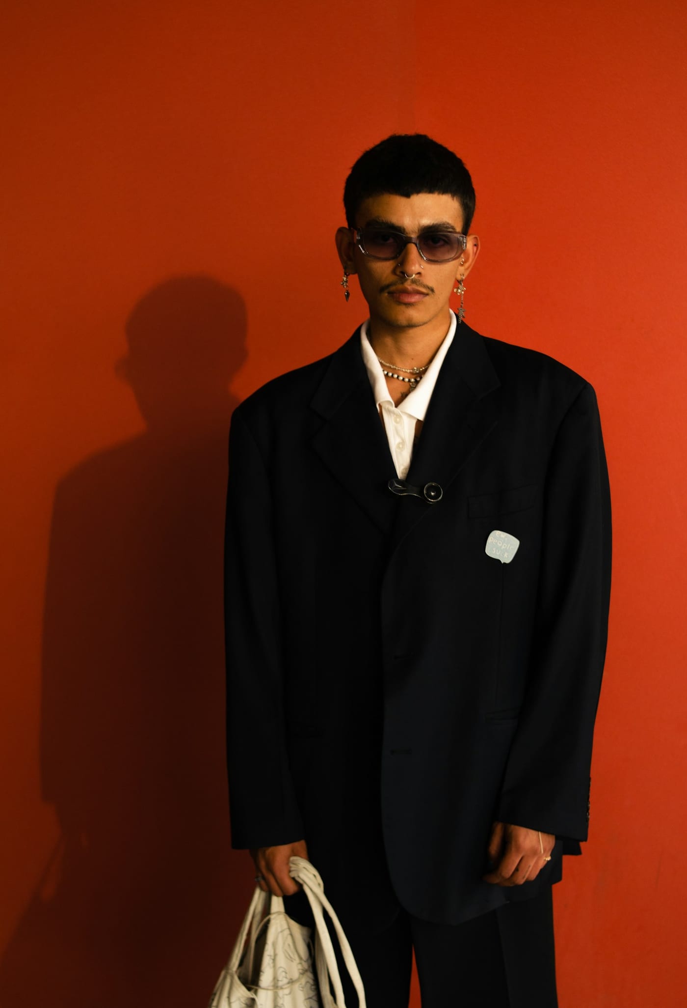 Man in an oversized black suit and tinted glasses against a red wall